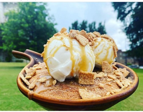 A wooden bowl filled with caramel sauce, topped with two scoops of vanilla ice cream and crushed cereal.