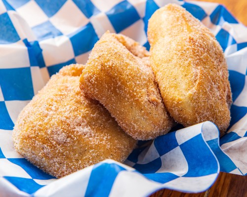 Three golden, sugar-coated pastries resting in a blue and white checkered basket.
