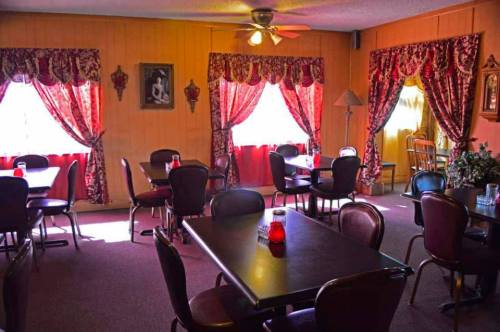 Cozy dining area with tables, chairs, and red curtains, featuring warm lighting and decorative accents.