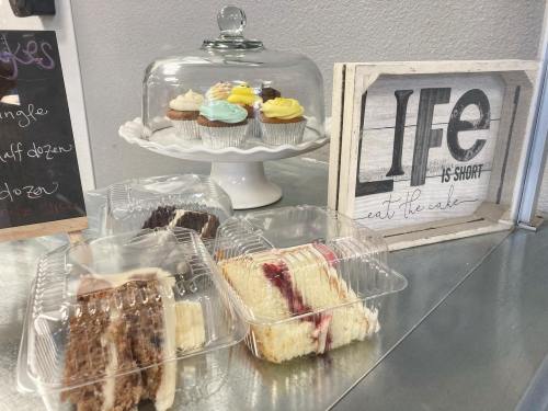 A display of cupcakes under a glass dome, with assorted cake slices in clear containers and a sign that says "Life is short, eat the cake."