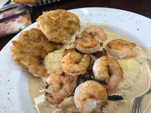 A plate of shrimp and grits topped with spices, accompanied by two crispy fried green tomatoes.