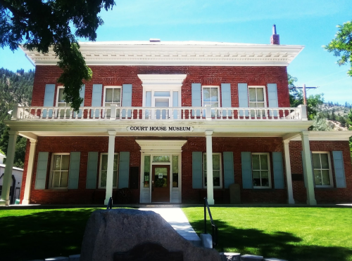 Historic brick building with a white balcony, labeled "Court House Museum," surrounded by green grass and trees.