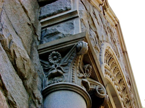 Close-up of a decorative stone column with floral motifs, set against a textured stone wall.