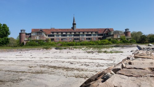 Historic building with a steeple, surrounded by greenery, set against a clear blue sky and sandy beach.