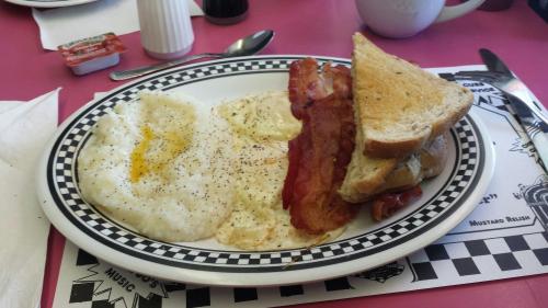 A plate of breakfast featuring two eggs, bacon, grits, and a slice of toast on a checkered plate.