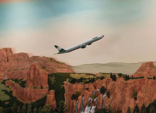 A model airplane flying over a scenic landscape with mountains and a waterfall.