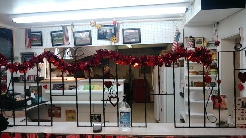 A decorated counter with red garlands and heart ornaments, featuring photos and a hand sanitizer station.