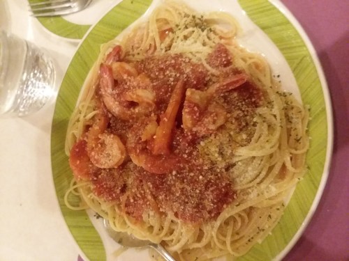A plate of spaghetti topped with shrimp in a tomato sauce, garnished with herbs and grated cheese.
