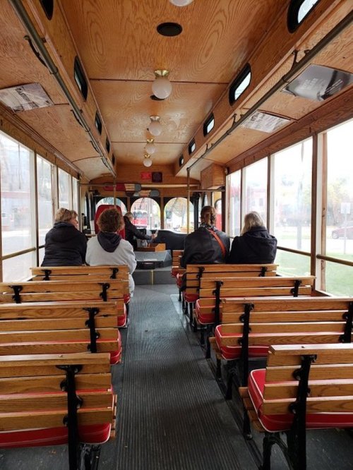 Interior of a vintage trolley with wooden benches, showing a few passengers seated and a view out the front windows.