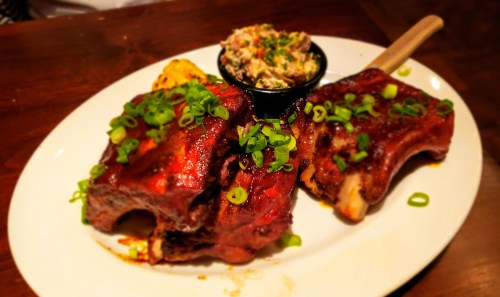 A plate of glazed ribs topped with green onions, served with a side of creamy coleslaw.