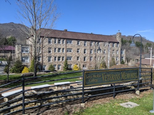 Stone building with a sign reading "Lees-McRae College Veterans Memorial" and mountains in the background on a clear day.