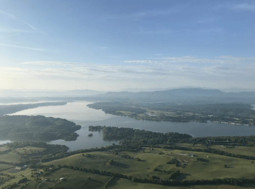 Aerial view of a serene landscape featuring a river, islands, and rolling green hills under a clear blue sky.