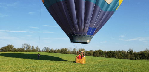 A colorful hot air balloon is landing in a green field, with a person standing nearby and a clear blue sky above.