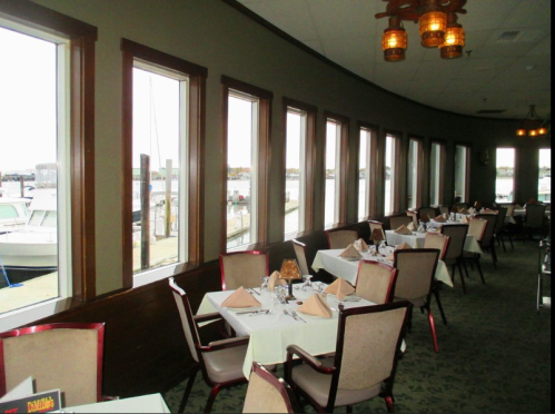 Interior of a restaurant with large windows overlooking a marina, featuring tables set for dining.