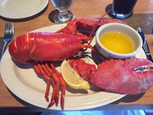 A cooked lobster on a plate with melted butter and a lemon wedge, served in a restaurant setting.