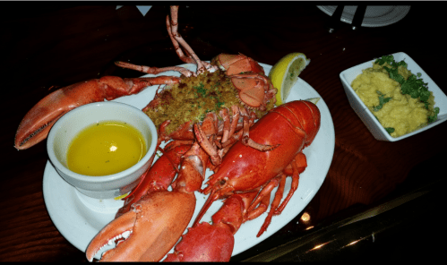 A plate of lobster with a side of melted butter and a small bowl of creamy dip, garnished with lemon.