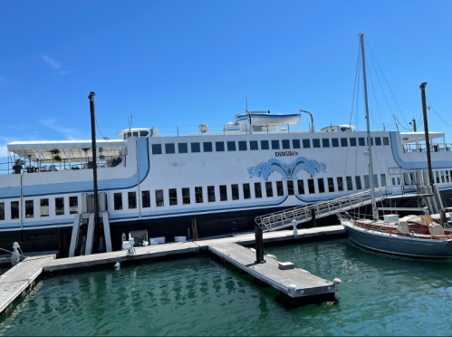 A large white boat docked at a marina under a clear blue sky, with another smaller boat nearby.