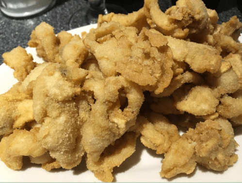 A plate of golden-brown fried food, likely seafood, with a crispy texture and irregular shapes.