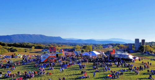 A vibrant outdoor festival scene with food trucks, crowds, and mountains in the background under a clear blue sky.