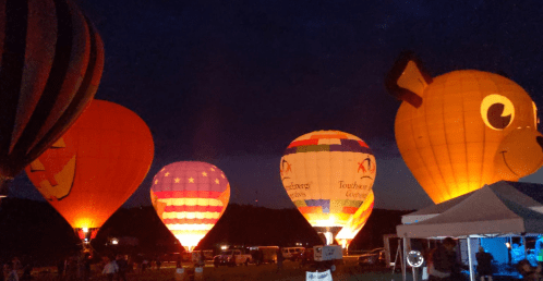 Colorful hot air balloons illuminated at night, with a bear-shaped balloon and a festive atmosphere.