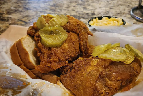 A close-up of a fried chicken sandwich topped with pickles, served with a side of macaroni and cheese.