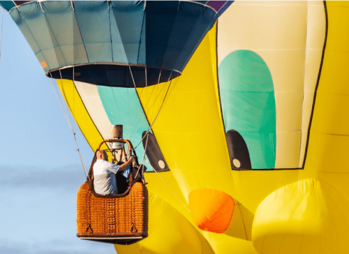 A colorful hot air balloon with a cartoonish face, featuring a wicker basket carrying two people.