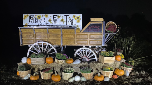 A wooden wagon decorated with flowers, pumpkins, and plants, promoting a fall trail at night.