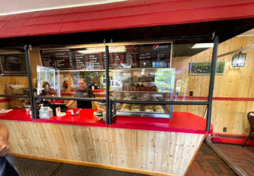 A cozy restaurant counter with a menu board, display case of baked goods, and staff serving customers.