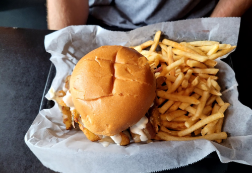 A close-up of a burger with a golden bun and fries on a tray, set on a dark table.