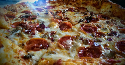 A close-up of a pepperoni pizza with melted cheese and toppings, illuminated by a bright light.