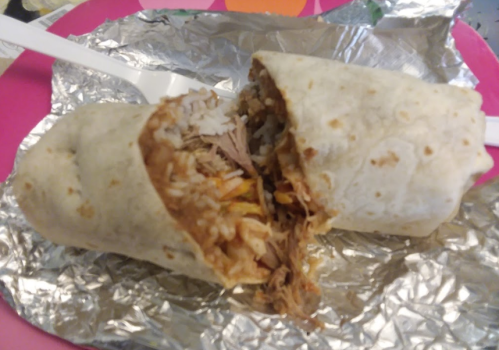 A partially unwrapped burrito filled with rice and shredded meat, resting on a pink plate with a plastic fork.