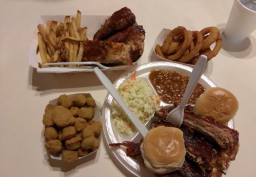 A spread of barbecue ribs, fries, onion rings, coleslaw, baked beans, and fried okra on a table.