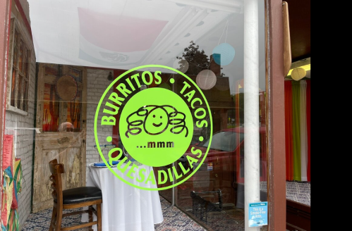 Bright green sign on a restaurant window featuring "Burritos, Tacos, Quesadillas" with a smiling face logo.