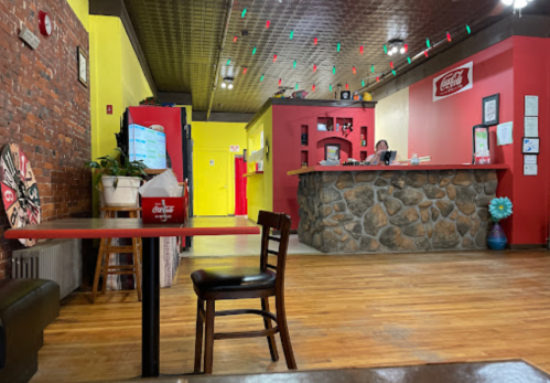A colorful restaurant interior with a stone counter, red tables, and a cozy atmosphere. A staff member is at the counter.