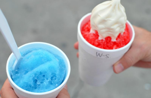 Two cups of shaved ice: one blue with a spoon, and one red topped with soft serve ice cream.