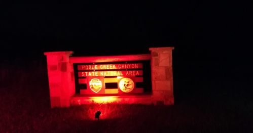 A illuminated sign for Pogue Creek Canyon State Natural Area at night, glowing red against a dark background.