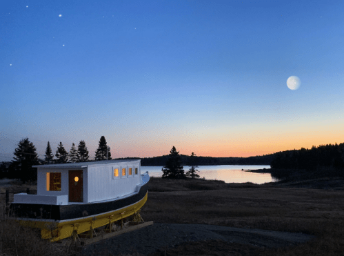 A boat-shaped structure sits on land at dusk, with a serene lake and a bright moon in the background.