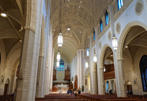 Interior of a grand church featuring tall arches, stained glass windows, and wooden pews. Soft lighting enhances the atmosphere.