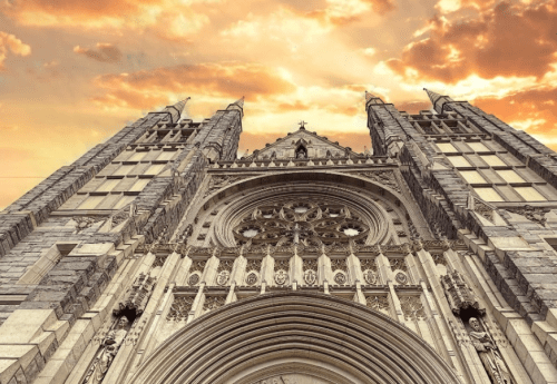 Gothic cathedral facade with intricate details, towering spires, and a dramatic sunset sky in the background.