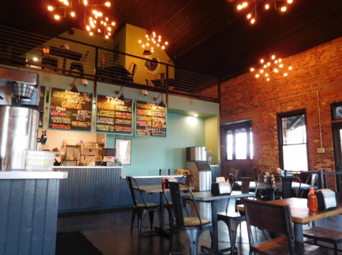 Interior of a cozy restaurant featuring wooden tables, a colorful menu board, and warm lighting.