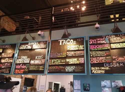A colorful menu board displaying various taco options and snacks in a casual dining setting.
