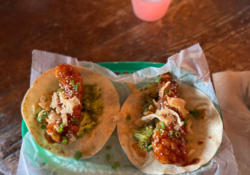 Two tacos filled with broccoli and crispy toppings, drizzled with a sweet sauce, served on a green tray.