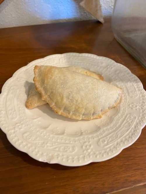 Two golden-brown empanadas on a decorative white plate, resting on a wooden surface.