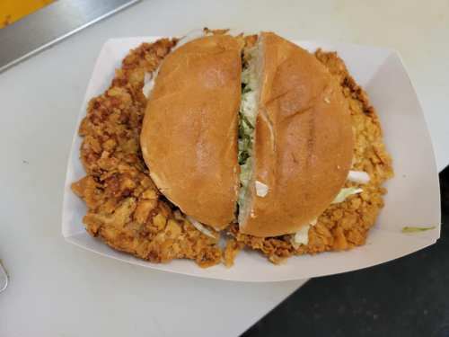 A split fried chicken sandwich on a bed of crispy fried chicken, with lettuce peeking out from the bun.