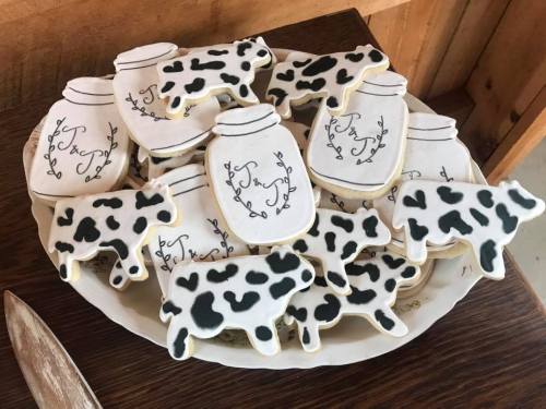 A plate of decorated cookies shaped like cows and jars, featuring black and white designs on a rustic wooden table.