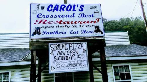 Sign for Carol's Crossroad Best Restaurant, featuring pizza specials and open hours, with a playful note about panthers.