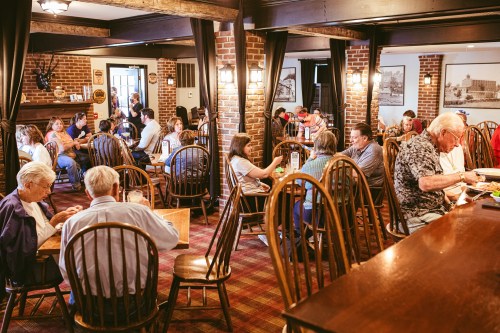 A busy restaurant interior with patrons seated at wooden tables, enjoying meals and conversing in a cozy atmosphere.