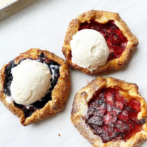 Three fruit tarts with ice cream on top, featuring berry and cherry fillings, on a baking sheet.