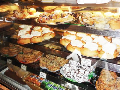 A display case filled with various baked goods, including cookies, pastries, and muffins topped with cream.