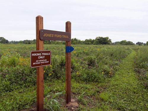 Signpost for Jones Ford Trail with a warning for hikers, surrounded by a grassy field under a cloudy sky.
